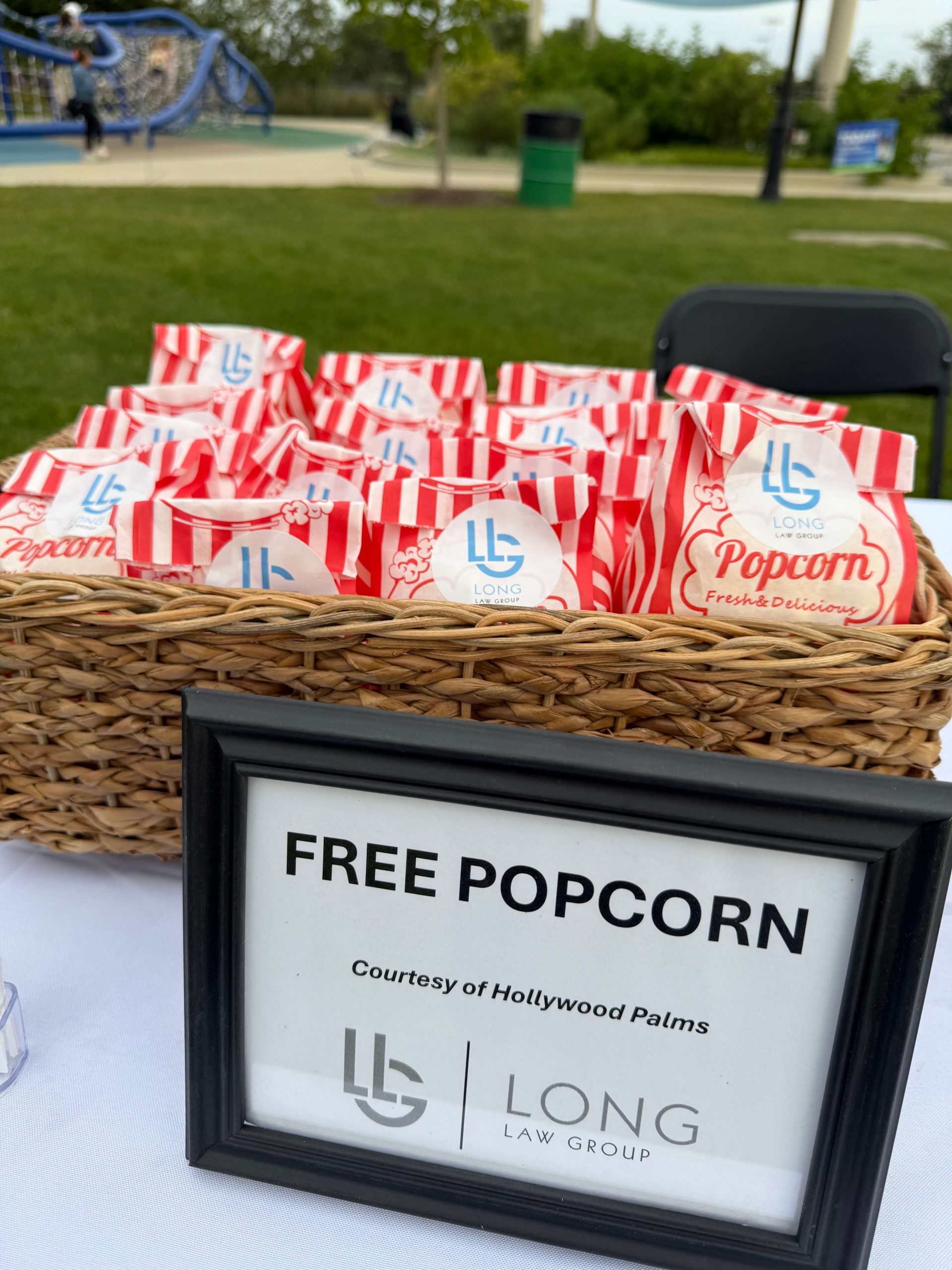Basket of branded popcorn bags with Long Law Group logo and Free Popcorn sign courtesy of Hollywood Palms at Naperville community event