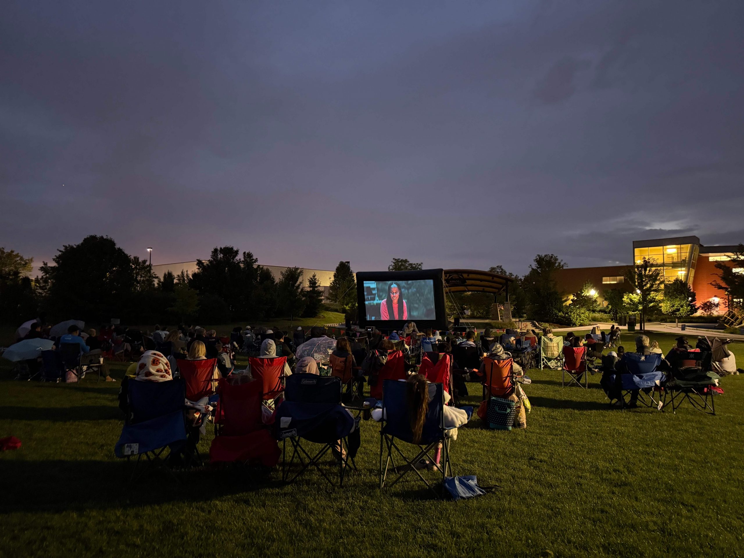 Families with lawn chairs watching outdoor movie screening at dusk in Naperville park sponsored by Long Law Group community involvement